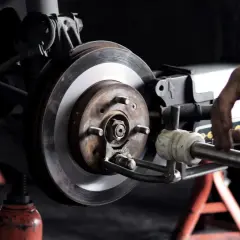 Mechaniker arbeitet an einer **Bremsscheibe**. Das Auto steht auf einem Wagenheber.