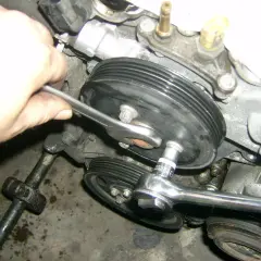 Hand mit Ratsche löst Wasserpumpenrad an einem Opel Corsa D Motor.