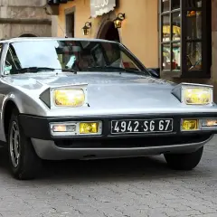 Silberner Simca Bagheera mit ausklappbaren Scheinwerfern fährt durch eine Gasse mit Kopfsteinpflaster.