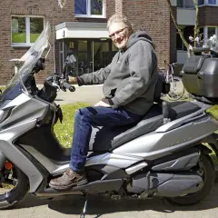 Mann auf silbernem Kymco New Downtown 350i, der über Probleme nachdenkt.