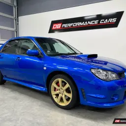 Blauer Subaru Impreza WRX mit goldenen Felgen und roter Bremsanlage steht in einer Garage.