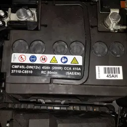 Batteriewechsel Hyundai ix20: Nahaufnahme einer 45Ah Autobatterie mit Warnsymbolen und technischen Daten.
