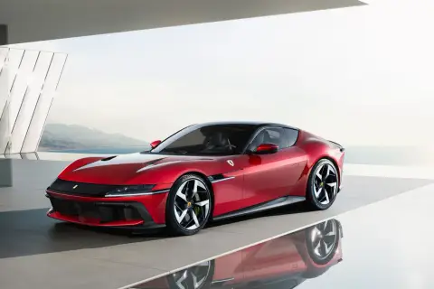 Roter Ferrari mit 12 Zylindern, elegant auf einer reflektierenden Fläche vor einer Küstenlandschaft.