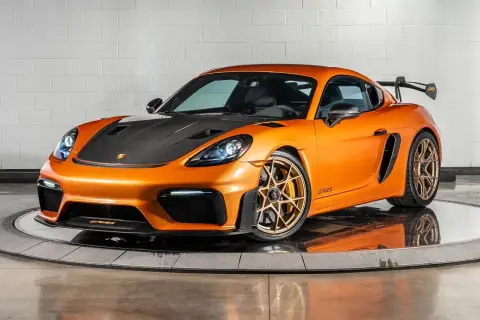 Orange Porsche GT4 RS mit Carbon-Motorhaube und goldenen Felgen, bereit für die Rennstrecke.