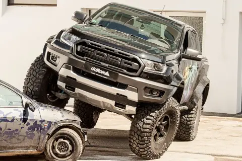 Schwarzer Ford Ranger mit **Ford Duratorq**-Motor überfährt ein kleines Auto. Offroad-Umbau mit riesigen Reifen.