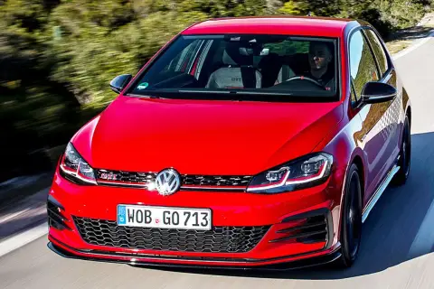 Roter Golf 7 GTI im Test auf einer kurvigen Straße, Fahrer im Inneren.