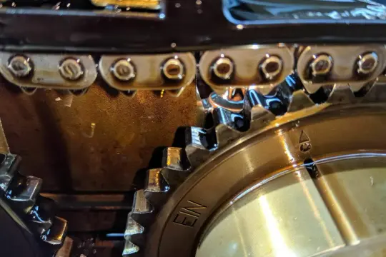 Detailaufnahme des Steuerkettentriebs eines Mercedes-Motors. Zahnräder und Kette sind mit Öl benetzt.