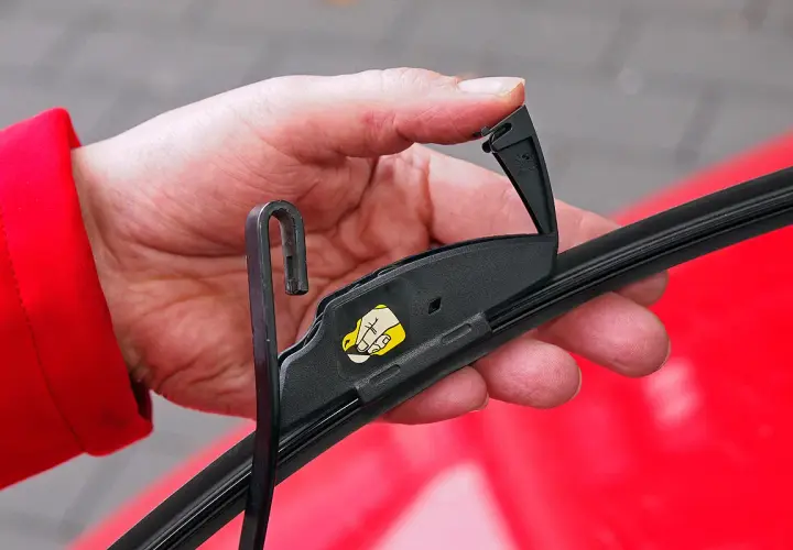 Hand wechselt Scheibenwischer vorne am Toyota Yaris. Der Wischerarm wird mit dem Haken eingehängt.