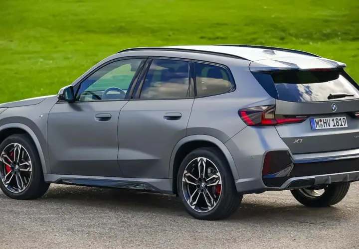Grauer BMW X1 23d steht auf Asphalt vor grüner Wiese.