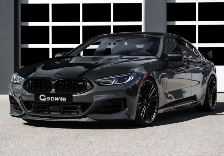 Ein getunter BMW M850 Gran Coupé in dunklem Grau mit Carbon-Elementen und auffälligem Heckspoiler steht vor einer Garage.
