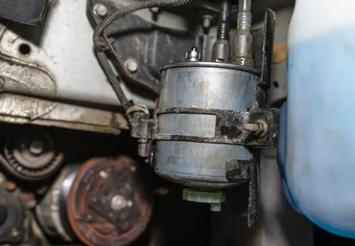 Nahaufnahme eines Kraftstofffilters, der neben einem blauen Behälter montiert ist. Mögliche kraftstoffpumpe defekt symptome könnten hier ihren Ursprung haben.