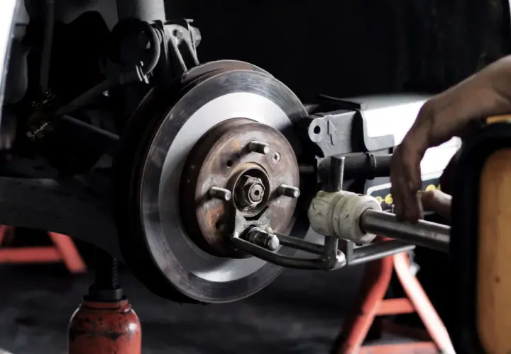 Mechaniker arbeitet an einer **Bremsscheibe**. Das Auto steht auf einem Wagenheber.