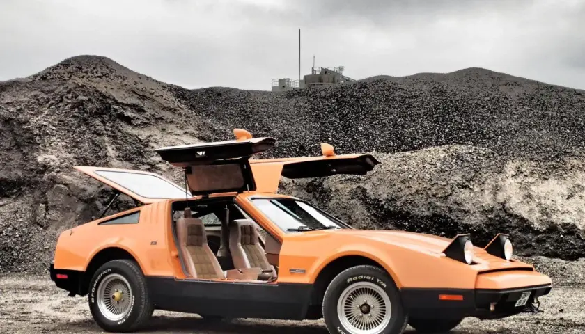 Orange Bricklin SV1 mit Flügeltüren steht auf Schotter vor einer Kiesgrube.