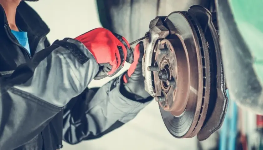 Mechaniker mit roten Handschuhen repariert eine festsitzende Bremse. Was tun? Werkstattarbeit.