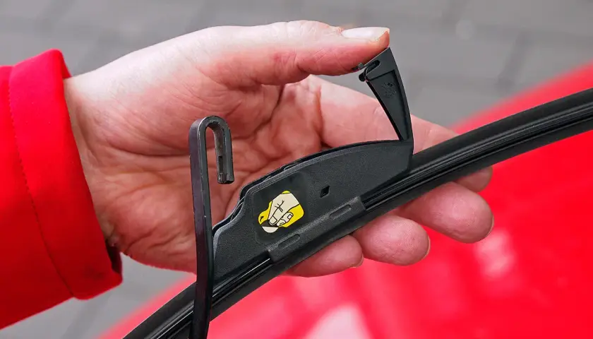 Hand wechselt Scheibenwischer vorne am Toyota Yaris. Der Wischerarm wird mit dem Haken eingehängt.