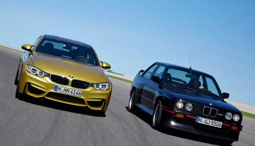 Goldener BMW M4 F80 und schwarzer BMW E30 M3 auf Rennstrecke.