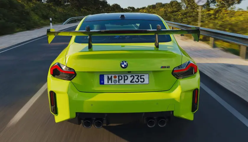 Leuchtend grüner BMW M2 Competition mit großem Heckspoiler rast auf einer Landstraße.