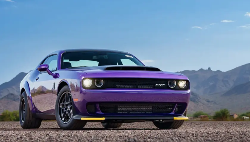 Lila Dodge Demon 170 mit gelben Akzenten steht auf Schotter vor einer Bergkulisse.
