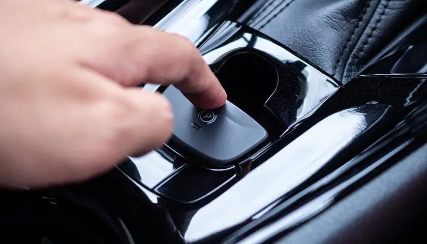 Ein Finger drückt auf den Knopf der elektronischen Handbremse. So funktioniert eine Handbremse im modernen Auto.