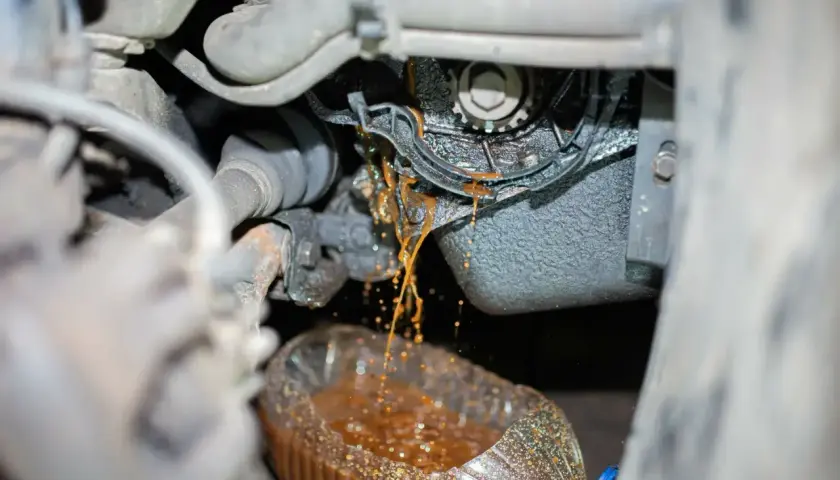 Flüssigkeit tropft aus dem Motorraum in eine Flasche. So merkt man das die Wasserpumpe defekt ist: Rostbraunes Kühlmittel tritt aus.