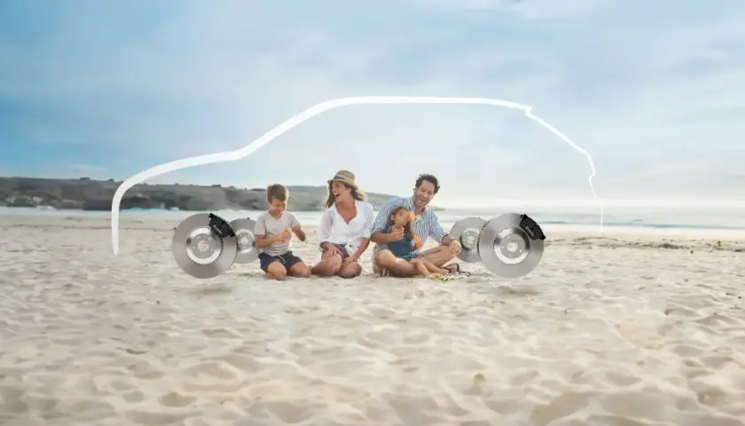 Familie am Strand sitzt neben Bremsscheiben, mit einer weißen Autokontur darüber.
