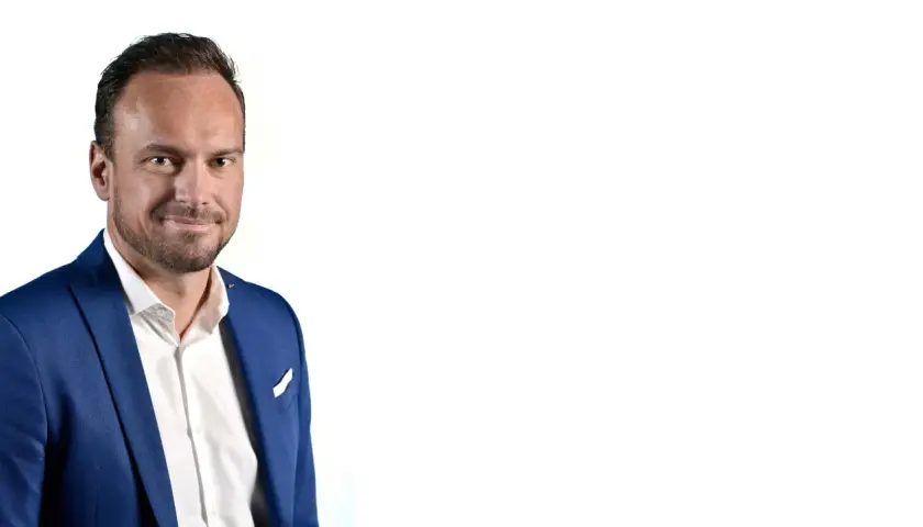 Markus Flasch, ein Mann mit Bart und blauem Anzug, lächelt in die Kamera.