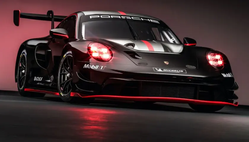 Porsche 992 GT3 R Rennwagen in Schwarz mit roten Akzenten und leuchtenden Scheinwerfern.