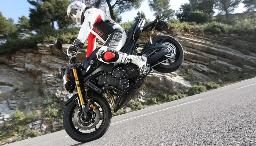 Motorradfahrer im Stunt, das Vorderrad in der Luft. Der Bremsweg des Motorrads ist hier irrelevant, da er gerade einen Wheelie macht.