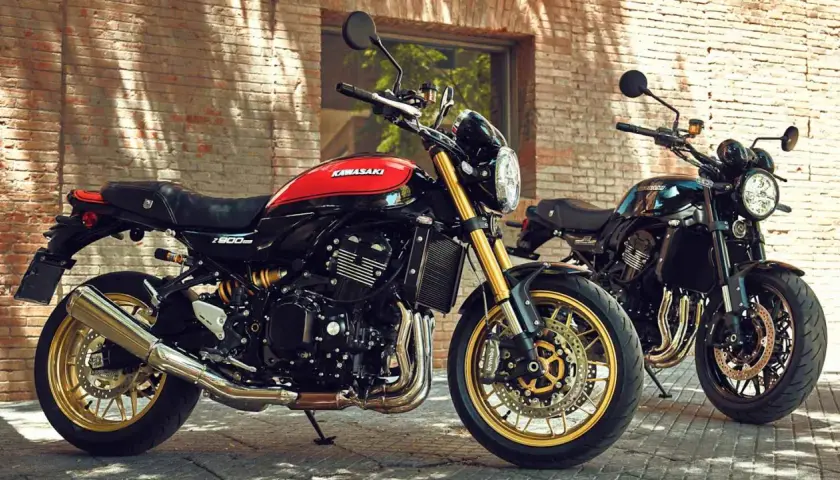 Zwei Kawasaki Z900RS, ein retro Motorrad in Schwarz-Rot, und ein weiteres in Schwarz, stehen vor einer Ziegelwand.