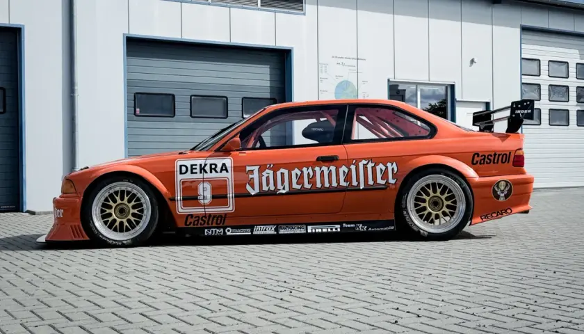 Orange BMW E36 Motorsport-Rennwagen mit Jägermeister-Lackierung und goldfarbenen Felgen.