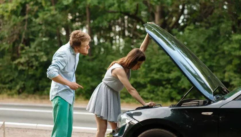 Mann zeigt auf Motorhaube, Frau schaut hinein. Sie fragt sich, ob sie mit einem abgassystem defekt weiterfahren kann.