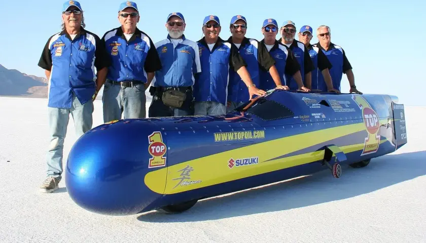 Ein Team steht stolz neben einem stromlinienförmigen Fahrzeug, das aussieht, als wäre es das schnellste Motorrad der Welt.