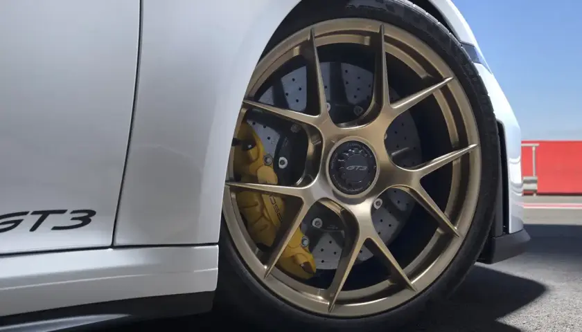 Porsche GT3 mit goldenen Felgen und gelben Bremssätteln. Die Keramik Bremsen Kosten sind hoch, aber die Leistung ist unschlagbar.