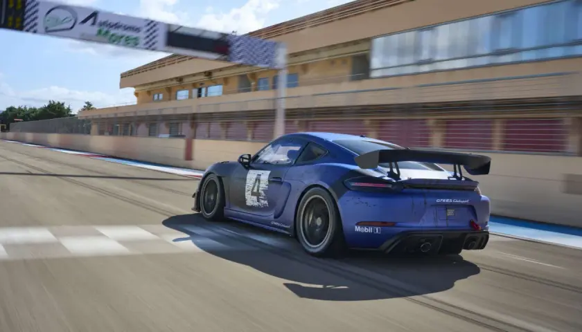 Blauer Porsche 718 Cayman GT4 Clubsport auf Rennstrecke, mit Start-/Zielbogen im Hintergrund.