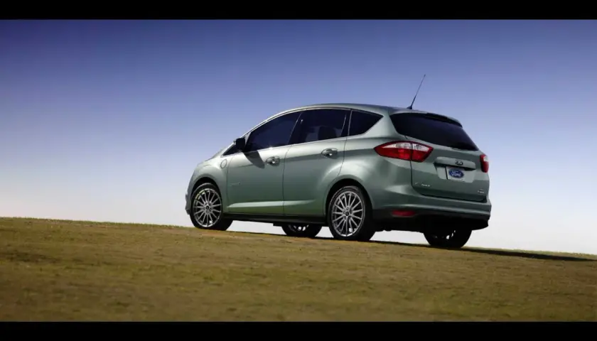Ein hellgrüner Ford C-Max Energi Plug-in Hybrid steht auf einem grasbewachsenen Hügel unter blauem Himmel.