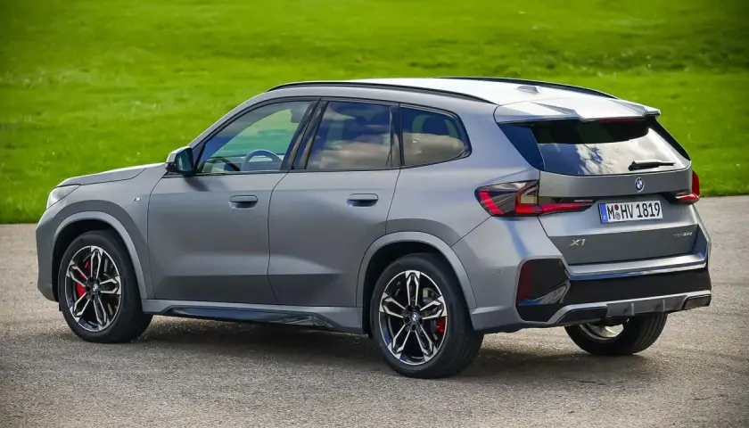 Grauer BMW X1 23d steht auf Asphalt vor grüner Wiese.