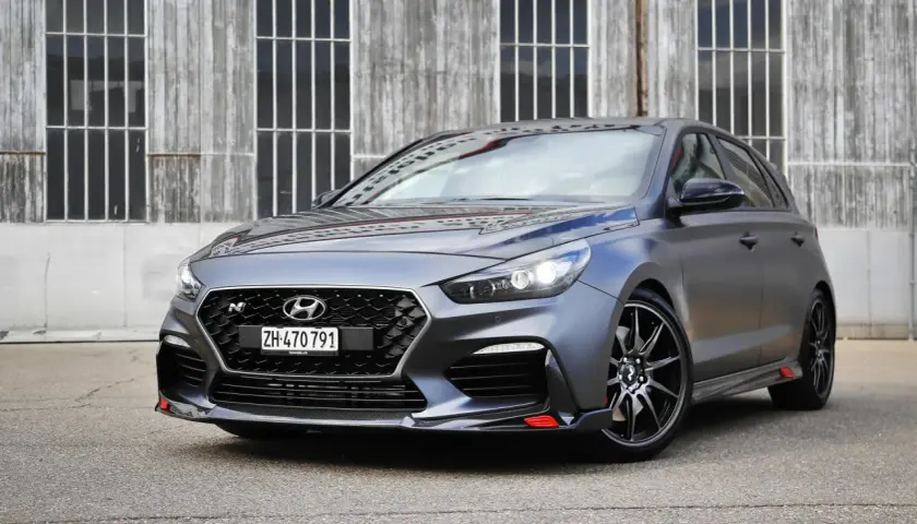 Grauer Hyundai i30 N Project C mit roten Akzenten vor Holzwand.