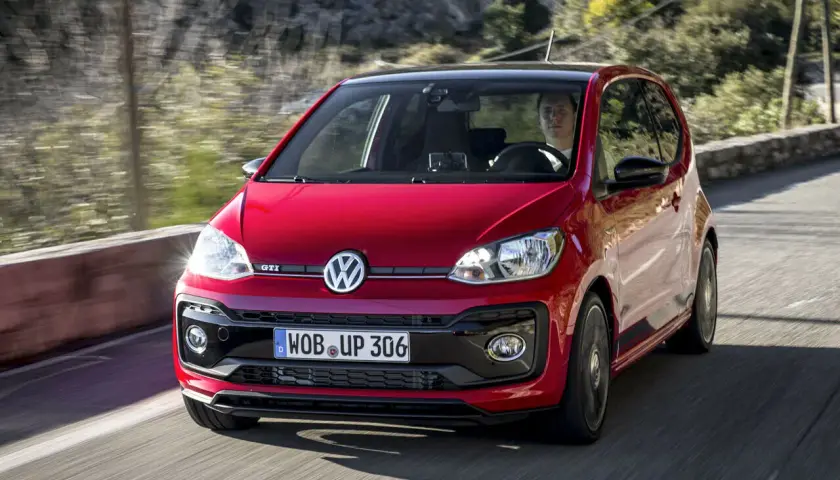 Roter VW Up GTI fährt auf einer kurvigen Straße mit Bäumen im Hintergrund.