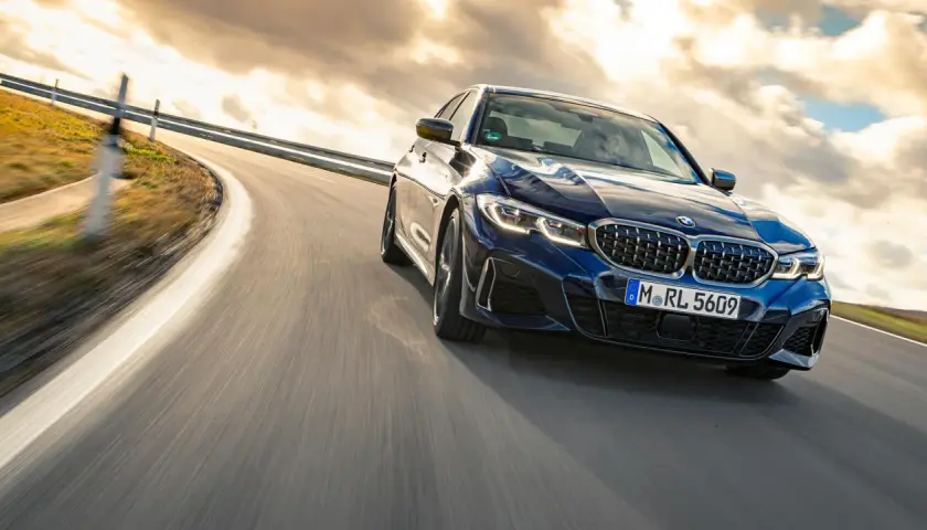 Blauer BMW M340i fährt auf einer kurvigen Straße bei Sonnenuntergang.