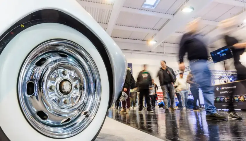 Detailaufnahme eines Oldtimer-Reifens mit Chromfelge auf einer motorsport expo. Besucher bewegen sich im Hintergrund.