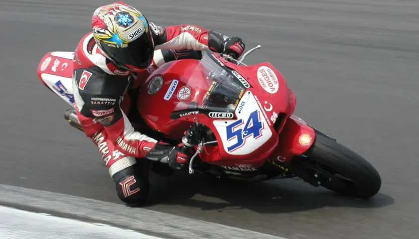 Rennfahrer Kenan Sofuoğlu in roter Lederkombi auf roter Yamaha mit Startnummer 54, in Schräglage auf der Rennstrecke.