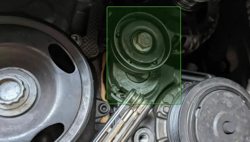 Detailaufnahme eines Keilriemenspanners und Riemenscheiben im Motorraum eines Autos.