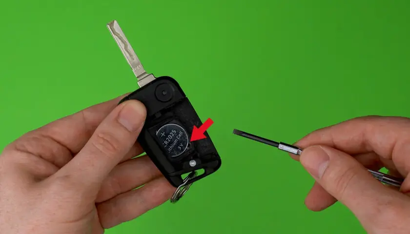 Schlüsselanhänger mit Batterie und Schraubendreher auf grünem Hintergrund.
