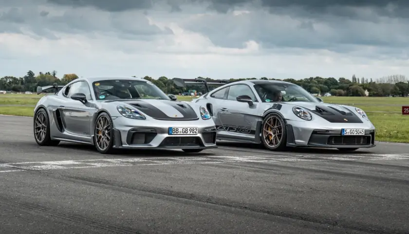 Zwei silberne Porsche GT4 und GT4 RS stehen nebeneinander auf einer Rennstrecke.
