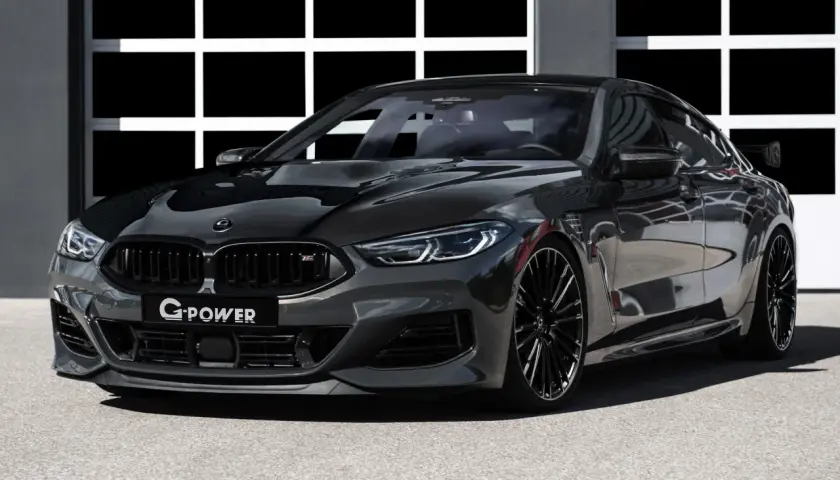 Ein getunter BMW M850 Gran Coupé in dunklem Grau mit Carbon-Elementen und auffälligem Heckspoiler steht vor einer Garage.