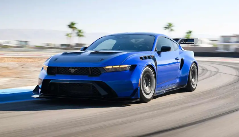Blauer Mustang GTD rast auf Rennstrecke, mit breiten Kotflügeln und großem Heckspoiler.