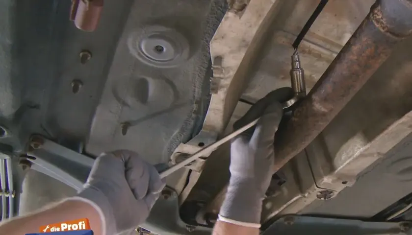 Hände mit Handschuhen wechseln die Lambdasonde an einem Ford Fiesta.