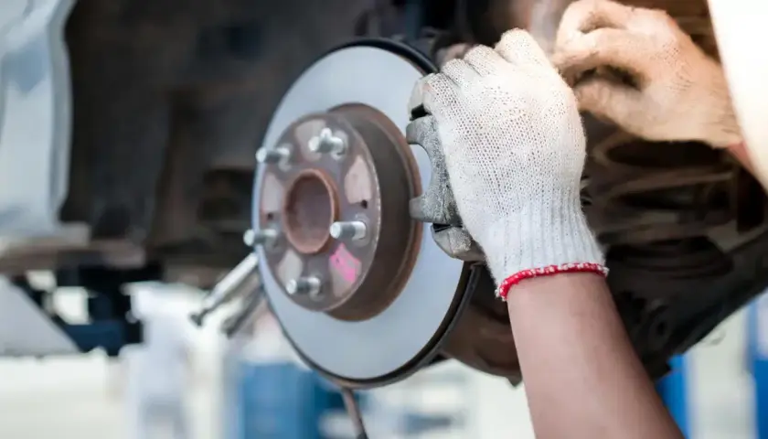 Hände in Handschuhen prüfen eine Bremsscheibe und den Bremssattel eines Autos.