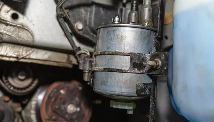 Nahaufnahme eines Kraftstofffilters, der neben einem blauen Behälter montiert ist. Mögliche kraftstoffpumpe defekt symptome könnten hier ihren Ursprung haben.