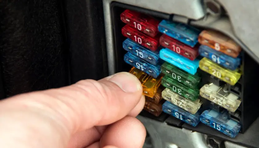 Hand prüft Sicherungen im Auto. So erkennt man eine defekte Sicherung: Der Draht im Inneren ist durchgebrannt.